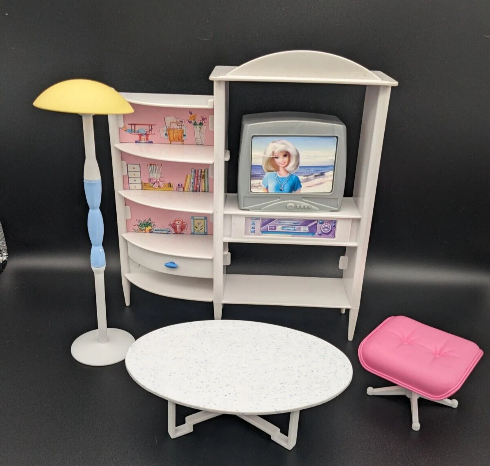 A 1990s Barbie living room setup, inclduing a TV stand with a television set, stick-on decorations, a mod floor lamp, a coffee table, and a pink cushioned stool